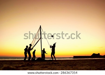 Silhouettes of a group of young people playing beach volleyball during sunset, on the beach in Brittany, France