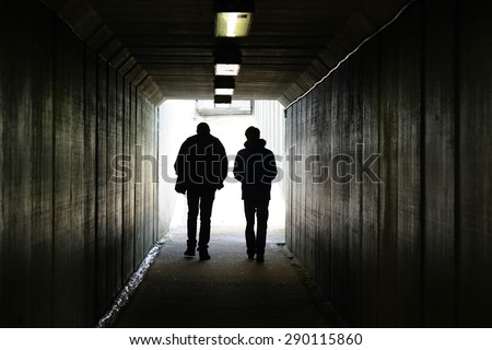 Two persons walk to the light in the end of the tunnel.