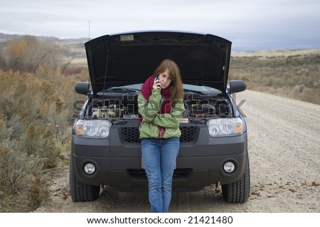 Teenage girl talking on a cell phone, trying to get help with her broken car.