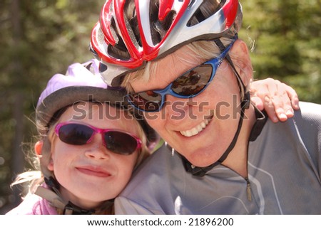 Mother and daughter in bicycle helmets. The daughter has her arm thrown around her mother.