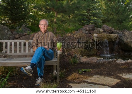Senior man sitting on a bench by a man-made pond and waterfall