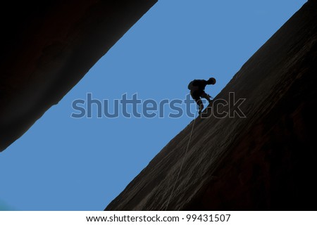Silhouette of rock climber rappelling a crack with blue sky behind.