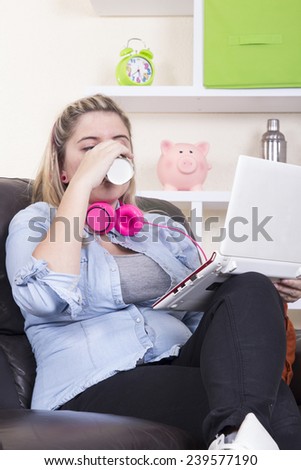 Blonde girl using computer on sofa and drinking coffee