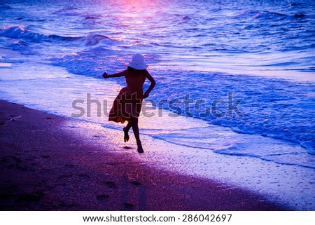 Girl running along the surf at sunset