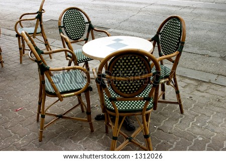 Small round table green and white patterned chairs sitting outside by the street.