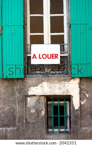French rental sign hangs in front of a window of a centuries old building. The interior has probably been renovated.