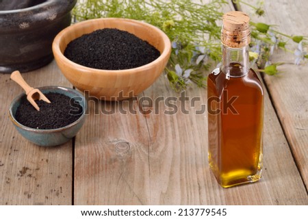 Nigella sativa oil in a bottle and nigella seeds and flowers on wooden background. Black cumin healing herb. Cold pressed, non refined oil. Traditional medicine.