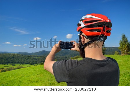 Cyclist taking pictures with smart phone. Caucasian man in bike helmet taking smartphone photo of mountains. Outdoor activity. Copyspace.