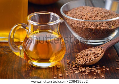 Brown flax seeds on spoon and flaxseed oil in glass jug on wooden table. Flax oil is rich in omega-3 fatty acid.