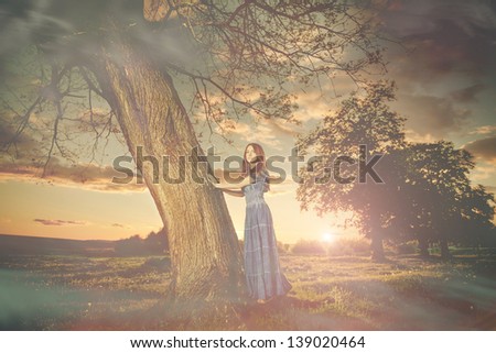 young lady in blue dress at spring meadow tree sunset