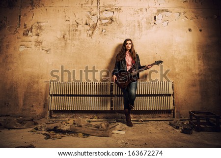 young caucasian woman with guitar at old dark room with cracked wall