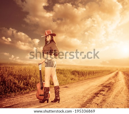 sexy cowgirl with guitar at rural sunset road