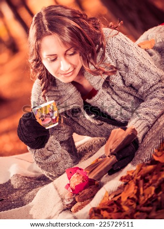 young lovely lady drinking tea and reading book at fall forest on plaid