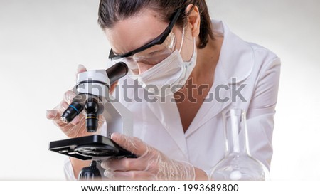 lab technician looks into the eyepiece of a microscope, a young female doctor or researcher in a white coat and face mask examines samples Сток-фото © 