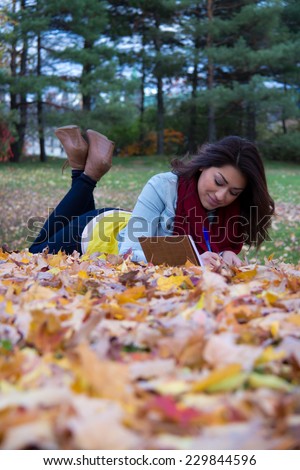 Girl writing in notebook while lying down on colorful fall leaves