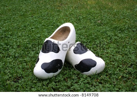 Wooden shoes with cow print standing on grass.