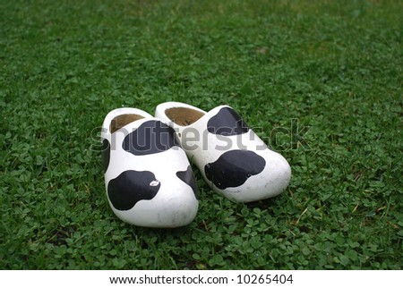 Wooden shoes with cow print standing on grass.