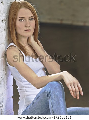 Portrait of a beautiful woman with red hair leaning against a white wall.