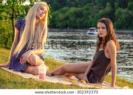Girl\'s picnic. Two pretty women are getting picnic on a blanket in a city park.