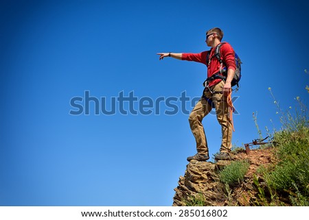 climber man with backpack on top of mountain pointing to sky