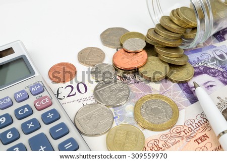 A finance still life with a jar of Sterling coins on Sterling notes, calculator and pen.