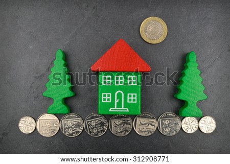 A toy house on Sterling coins and on a slate background.
