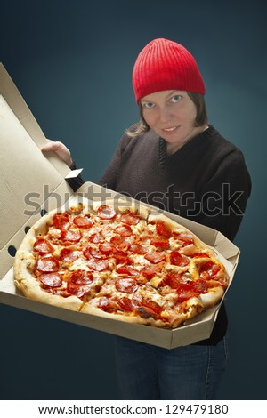 Pizza delivery worker woman in red cap, showing big pizza ,selective focus on pizza.