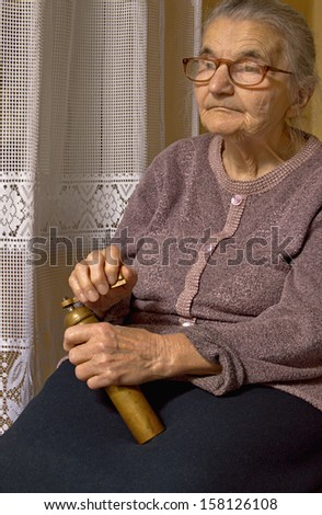 Portrait of an old woman with grinder in hands. Dreaming the past.