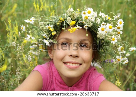 Cheerful preteen girl in field flower garland on green grass background