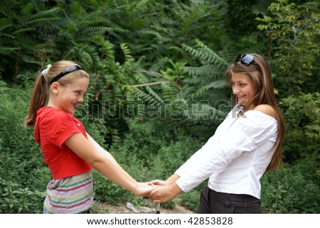 Two beautiful cheerful teenage girls holding hands outdoors