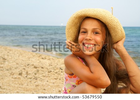 Cheerful preteen girl in straw hat enjoying sun-bath on sea beach