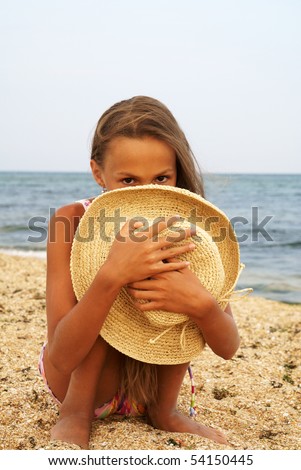 Portrait of cheerful preteen girl in straw hat enjoying sun-bath on sea beach