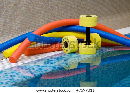 Aqua aerobics equipment. Noodles dumbbells for aqua aerobics lie on the coast in pool