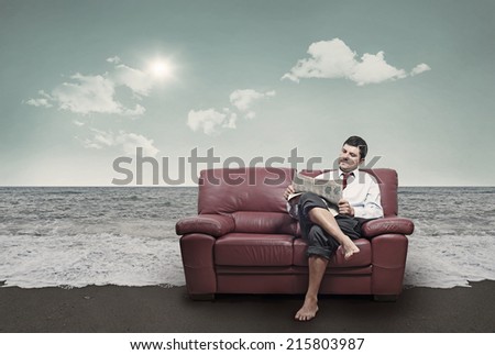 In a beach a man sitting on a red sofa while reading the newspaper