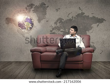A man sitting on a sofa holding a pc observe an illuminated globe (Elements of this image furnished by NASA)