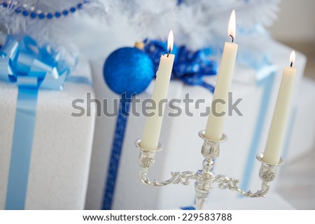 candlestick, three long candles, white Christmas tree with blue toys, garlands, beads, boxes, gifts
