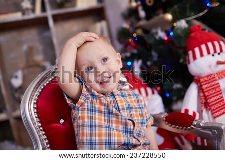active, cheerful kid is sitting in a chair near the Christmas tree