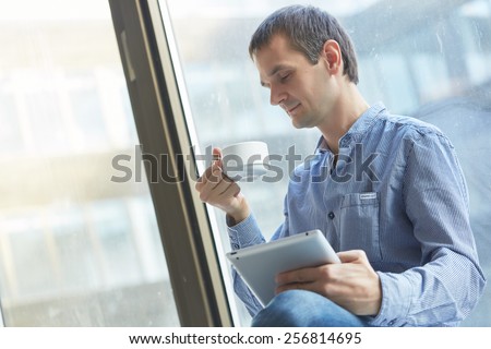 businessman with a cup of coffee and with the tablet at the window