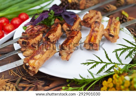 Three skewers with grilled ribs lie on a white plate with cherry tomatoes, onion and herbs