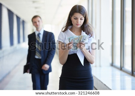 Business woman counts the money, businessman stands with tablet