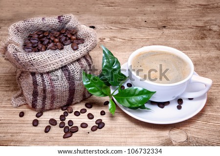 Cup of coffee with coffee beans in a beautiful brown bag, green branch of a coffee plant