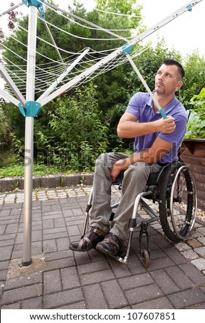disabled young man in wheelchair works outside on rotary clothes dryer
