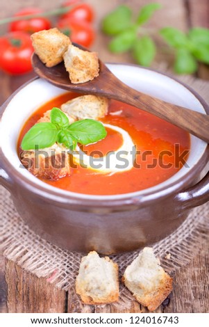 fresh tomato soup with basil thyme and raw tomatoes with bread pieces in a bowl on wooden background, ready to eat