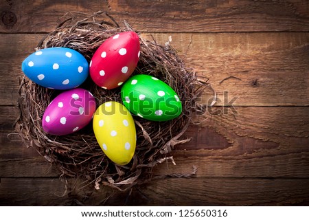 Colorful easter eggs with white points in straw nest on a wooden table