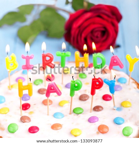 funny colorful birthday cake with candles and a red rose in background, happy birthday cake