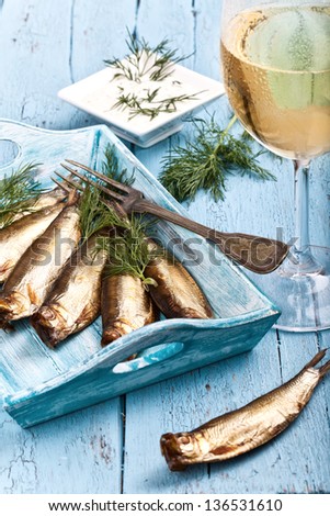fresh smoked sprats on a tray with fresh herbs and mayonnaise and a glass of white wine, ready for diner