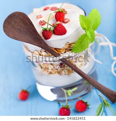 fresh cereal muesli with yogurt and wild strawberries in a glass with wooden spoon