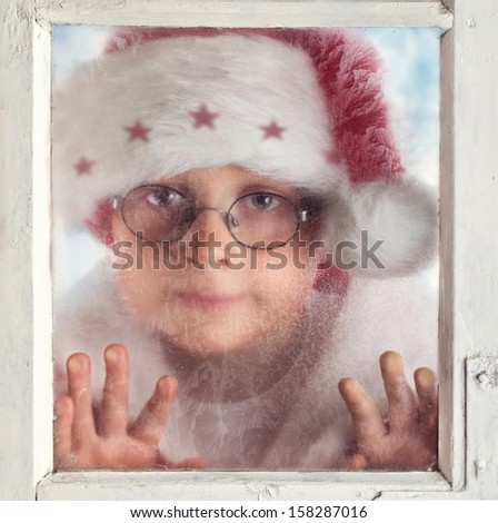 boy with Santa hat looking through snowy window, waiting for santa claus