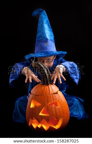 boy in blue witch\'s hat and costume with big pumpkin, a little wizard on Halloween