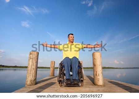 Happy handicapped man on a wheelchair on wooden boardwalk at lake on sunny summer day